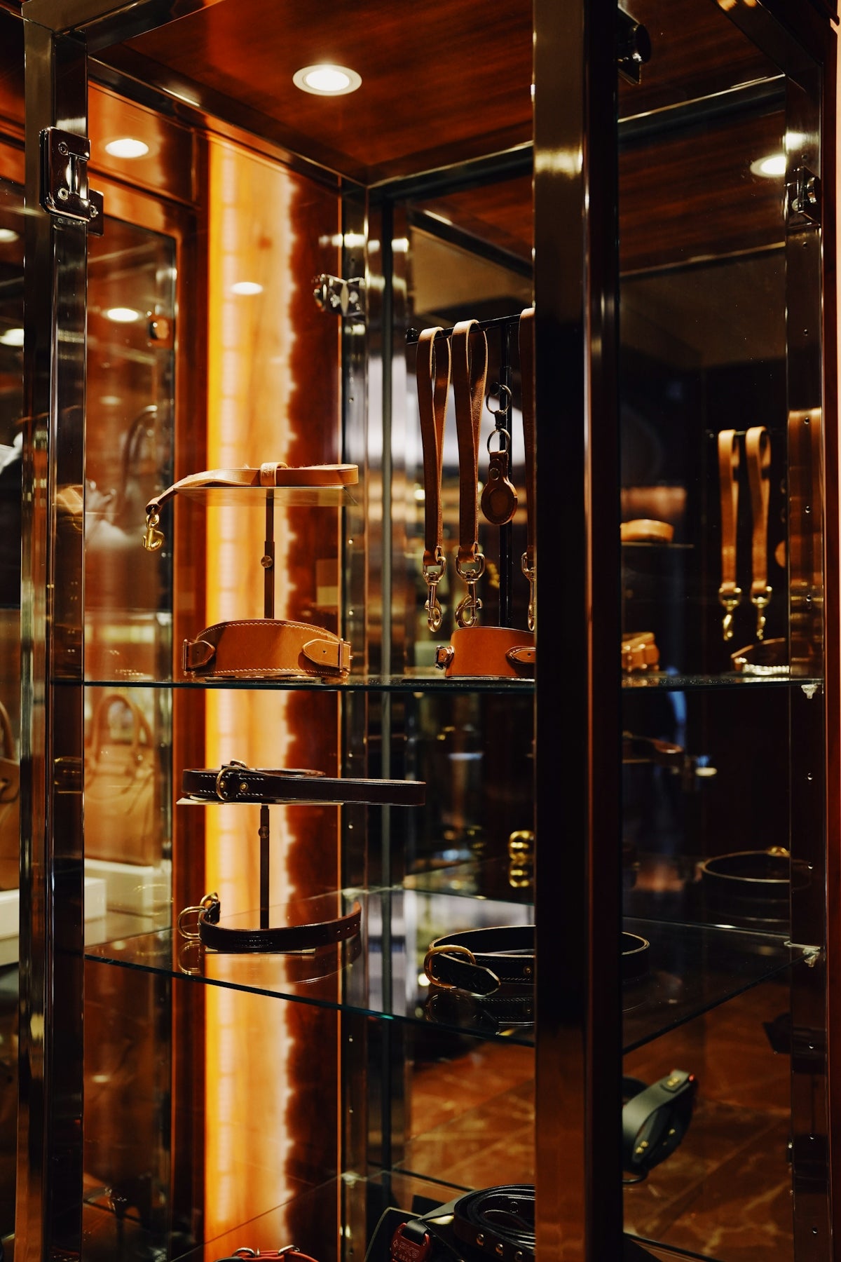 Leather belts and collars displayed on stands inside a glass retail cabinet